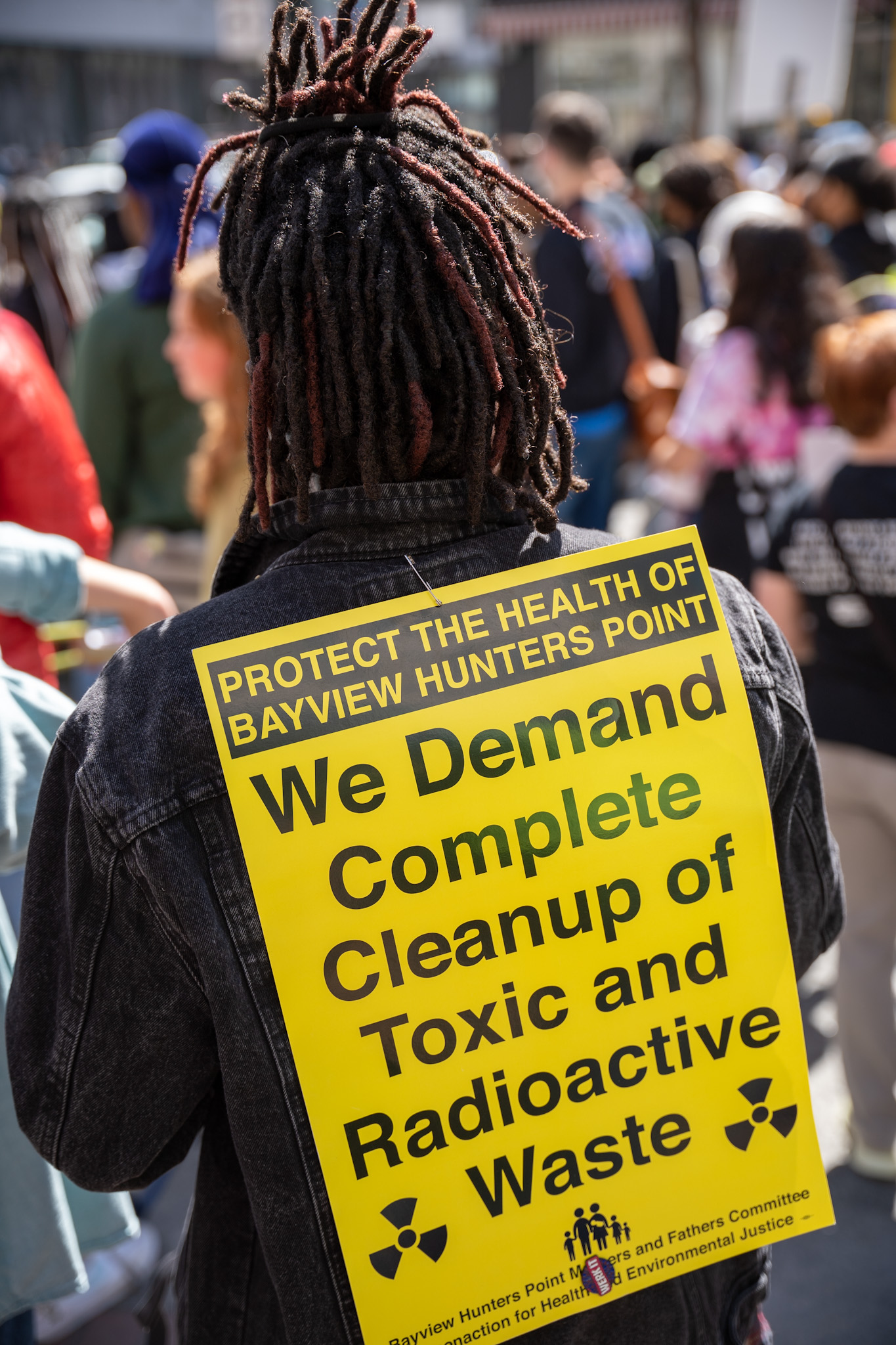 Protestor will yellow sign on their back reading "We demand complete cleanup of toxic and radioactive waste"